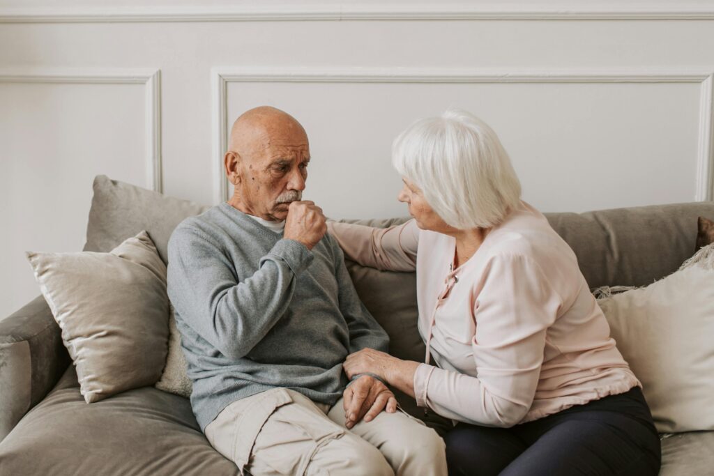 pexels-photo-5790716-5790716 An elderly woman comforts a man coughing on a couch, showcasing care and affection.